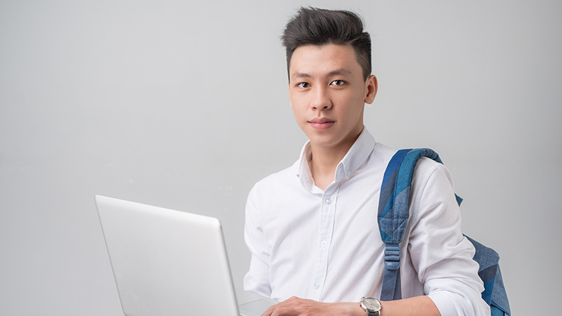 Happy casual asian male student using laptop isolated on a gray background